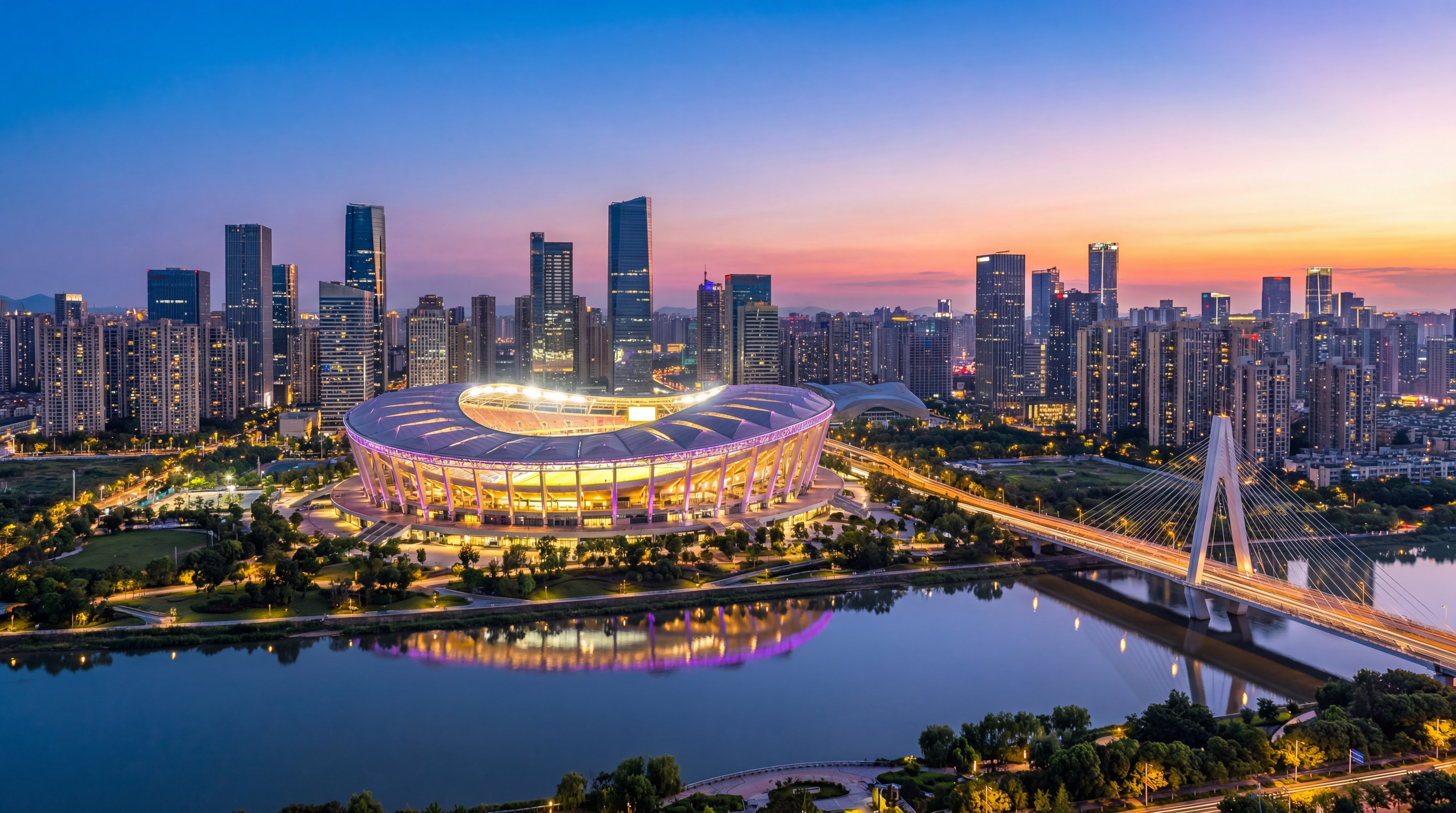 Stadium, high-rise towers and a cable-stayed bridge at dusk